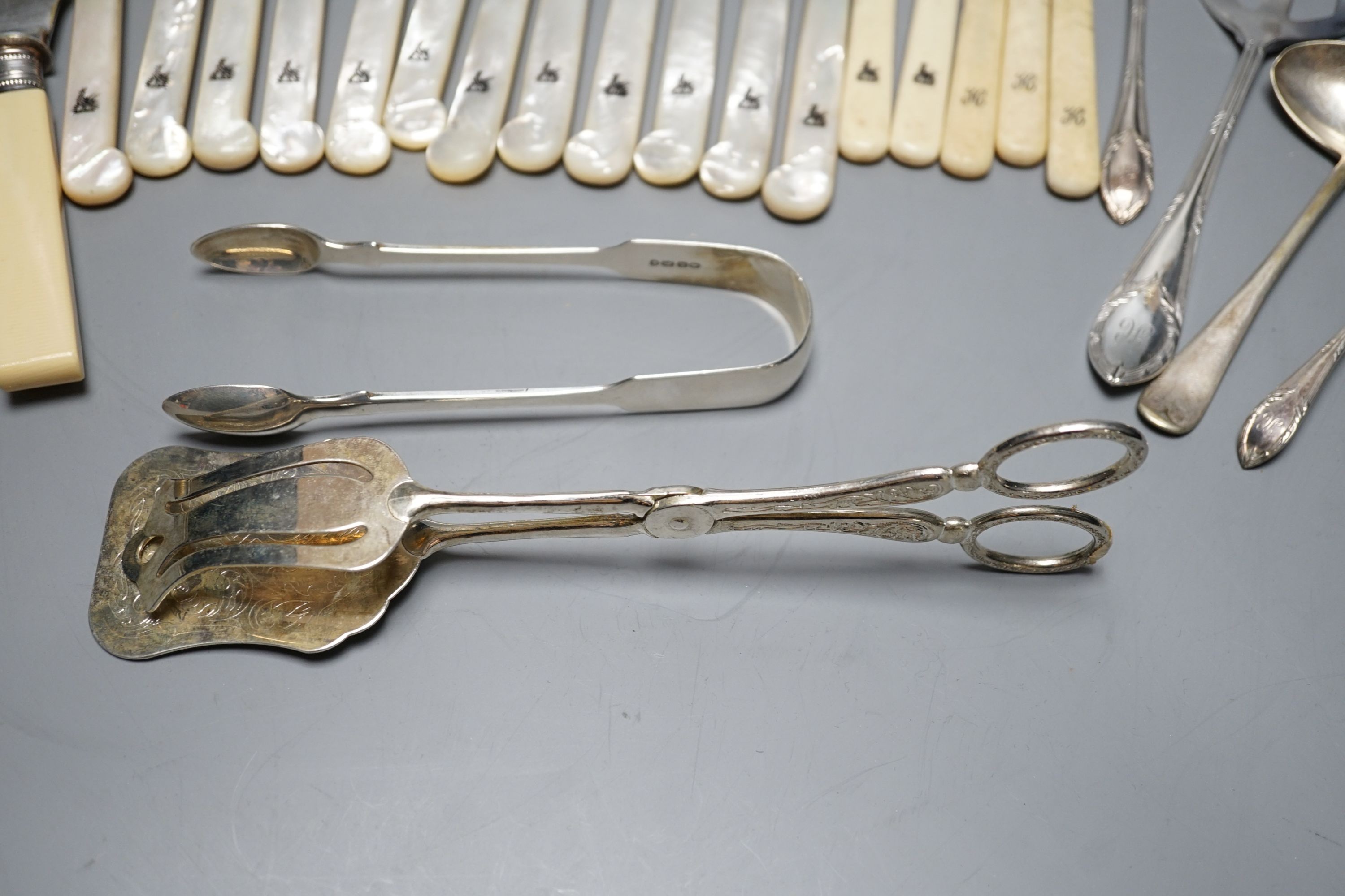 Six pairs of George V mother of pearl handled silver dessert eaters, George Howson, Sheffield, 1921, a pair of silver sugar tongs and assorted plated flatware.